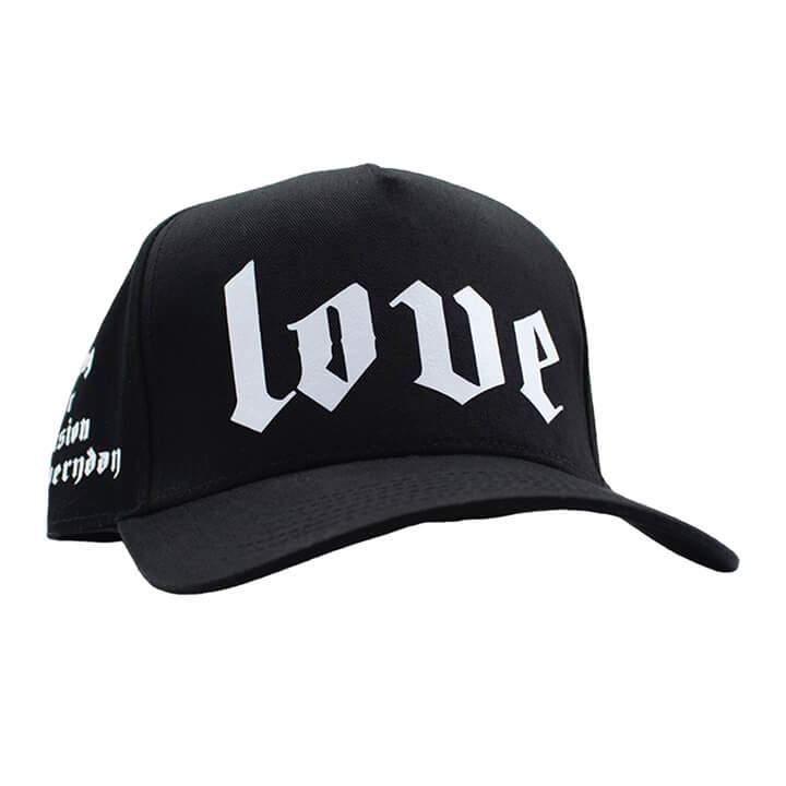 Slanted view of Classic black premium trucker hat with bold white printed 'LOVE' logo on the front panel and mesh back.