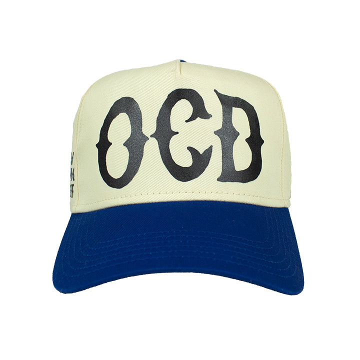 Front of Premium natural and royal blue trucker hat with Black printed 'OCD' acronym, standing for Obsessive Clothing Disorder.